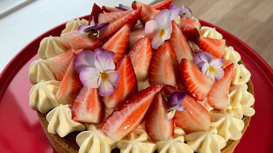 En jordbærtærte med creme, friske jordbær og blomster