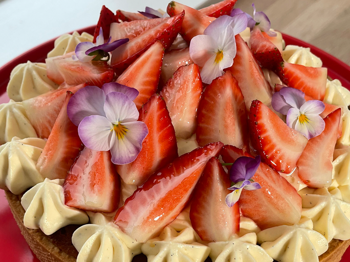 En jordbærtærte med creme, friske jordbær og blomster